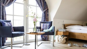 Une chambre moderne avec un lit, deux fauteuils, une petite table et une fenêtre avec des rideaux.