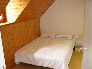 A small, single-bed room with wooden walls and a sloped ceiling.