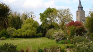 A garden with a variety of trees and shrubs, a lawn, and a distant church tower.