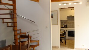 A staircase leading to a second floor, a kitchen area with basic appliances, and a dining area with chairs and a table.