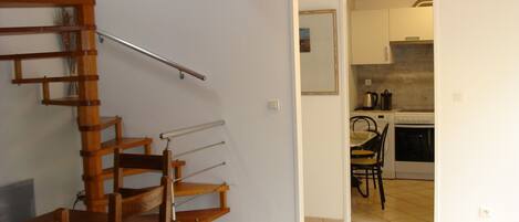 A staircase leading to a second floor, a kitchen area with basic appliances, and a dining area with chairs and a table.