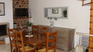 A dining area with a wooden table and chairs, a stone wall, a television, and a mirror above a counter.