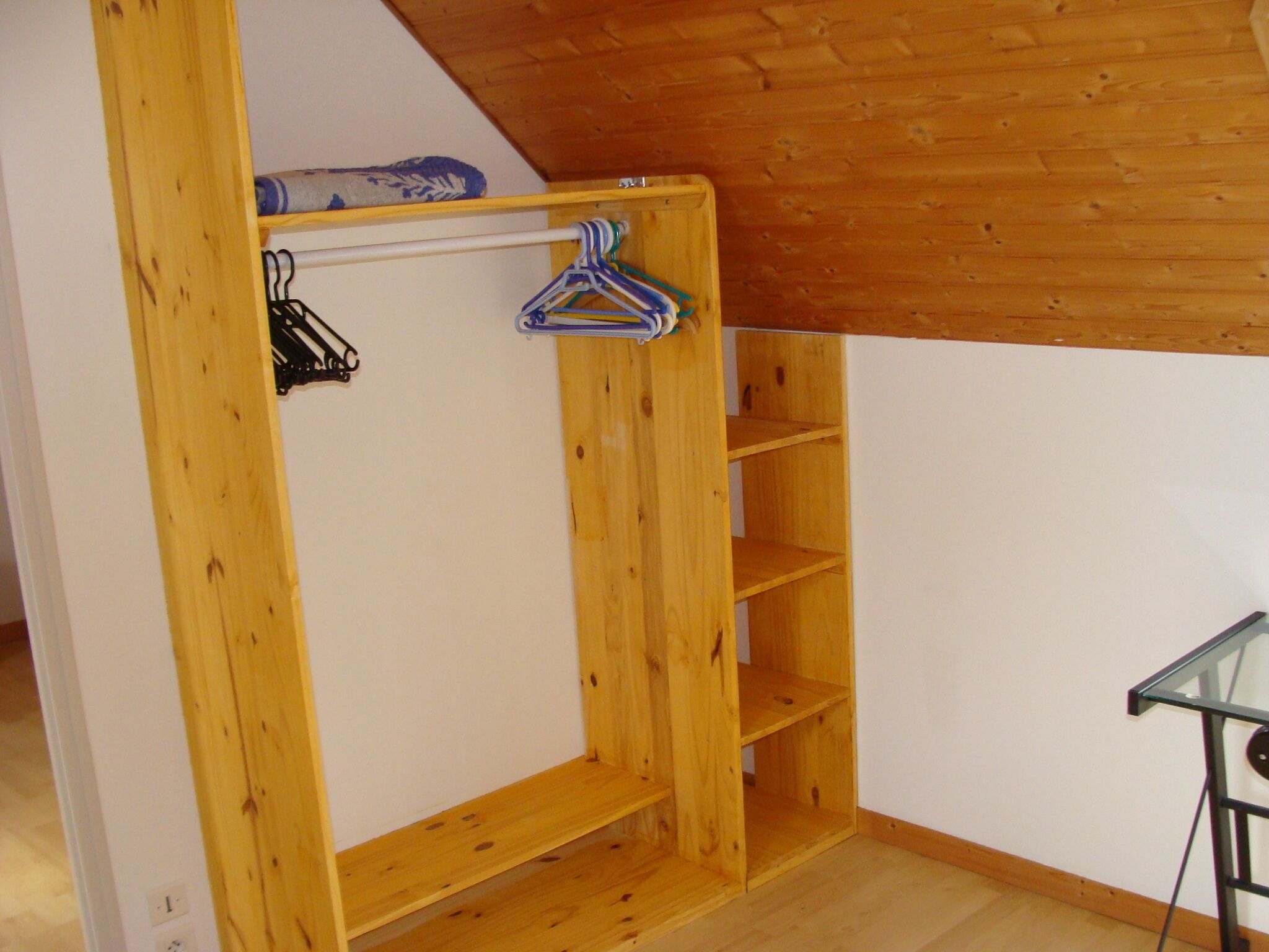 A room with a wooden wardrobe, a glass table, and a hanging rack.