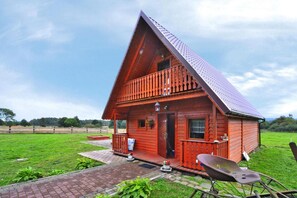 A wooden house with a sloped roof, a porch, and a paved entrance. - Holiday Home in Swiecianowo near Lake Beach (Swiecianowo)