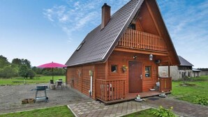 A wooden cabin with a sloped roof, a balcony, and a paved patio area. - Holiday Home in Swiecianowo near Lake Beach (Swiecianowo)