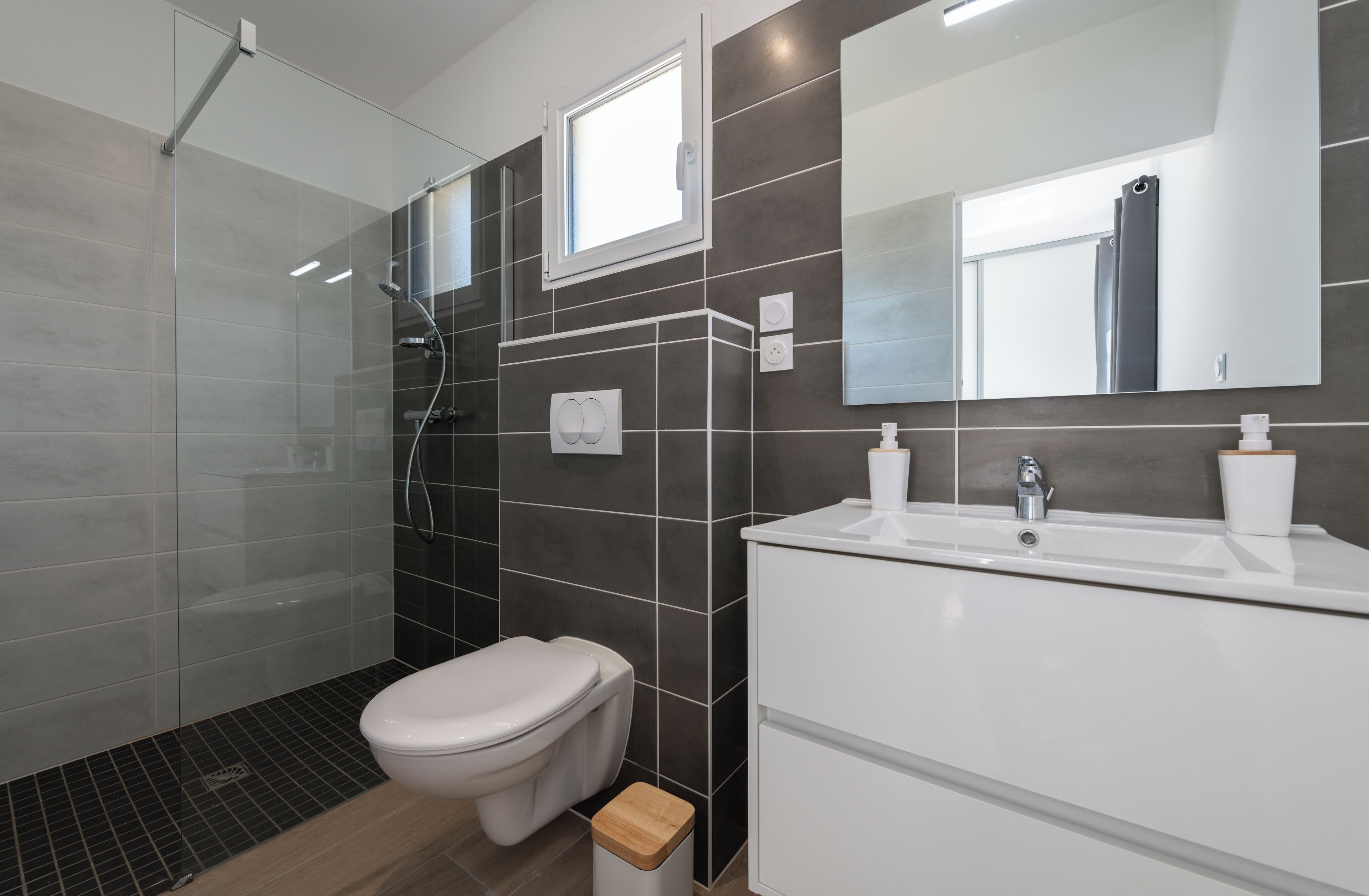 Une salle de bain moderne avec une douche à parois de verre, des toilettes, un lavabo avec un miroir et une petite fenêtre.
