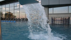 Une piscine dans laquelle de l’eau jaillit d’une structure surplombante, le tout étant entouré d’un bâtiment moderne doté de grandes fenêtres.