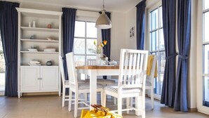 Un coin repas avec une table blanche, des chaises et un meuble blanc avec des étagères.