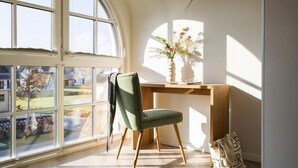 Une pièce avec une grande fenêtre, un bureau orné d’un vase de fleurs et une chaise.