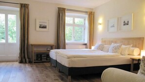 Habitación de hotel con cama doble, mesita de noche, una silla y ventana con cortinas.