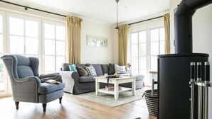 A living room with a sofa, armchair, and a black wood stove. - Haus in Bodstedt mit Sauna am Bodden (Fuhlendorf)