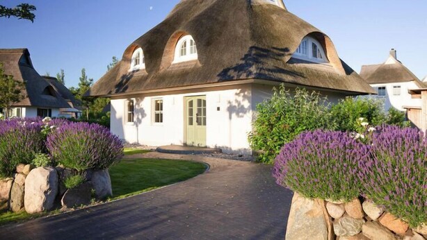 A house with a thatched roof, a green door, and a well-maintained lawn with lavender bushes. - Haus in Bodstedt mit Sauna am Bodden (Fuhlendorf)