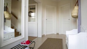 A hallway with white doors, a bench with a red bag, and a wicker basket on the wall. - Haus in Bodstedt mit Sauna am Bodden (Fuhlendorf)