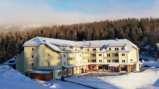 Un hôtel à plusieurs étages, dont le toit est recouvert de neige, et qui est entouré d’une forêt.
