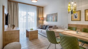 Un salon moderne avec un canapé, une table à manger et des chaises. On y trouve un téléviseur posé sur un meuble en bois et une lampe sur une table d’appoint.