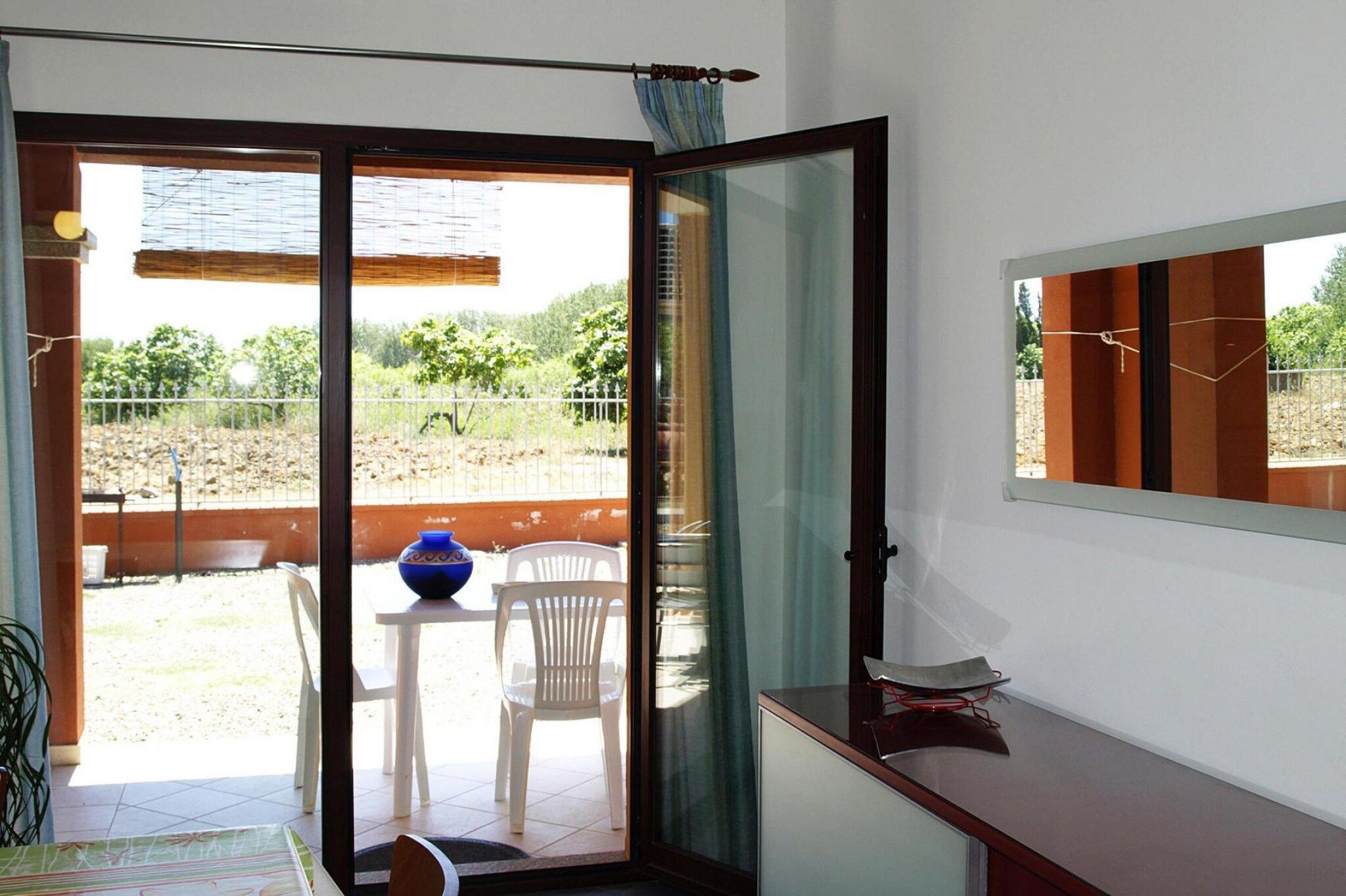 A room with a sliding glass door leading to an outdoor area with a table, chairs, and a decorative vase.