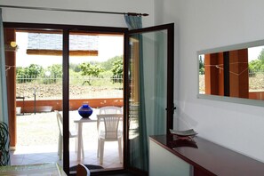 A room with a sliding glass door leading to an outdoor area with a table, chairs, and a decorative vase. - Apartment in a seaside resort (Domus De Maria / Chia)
