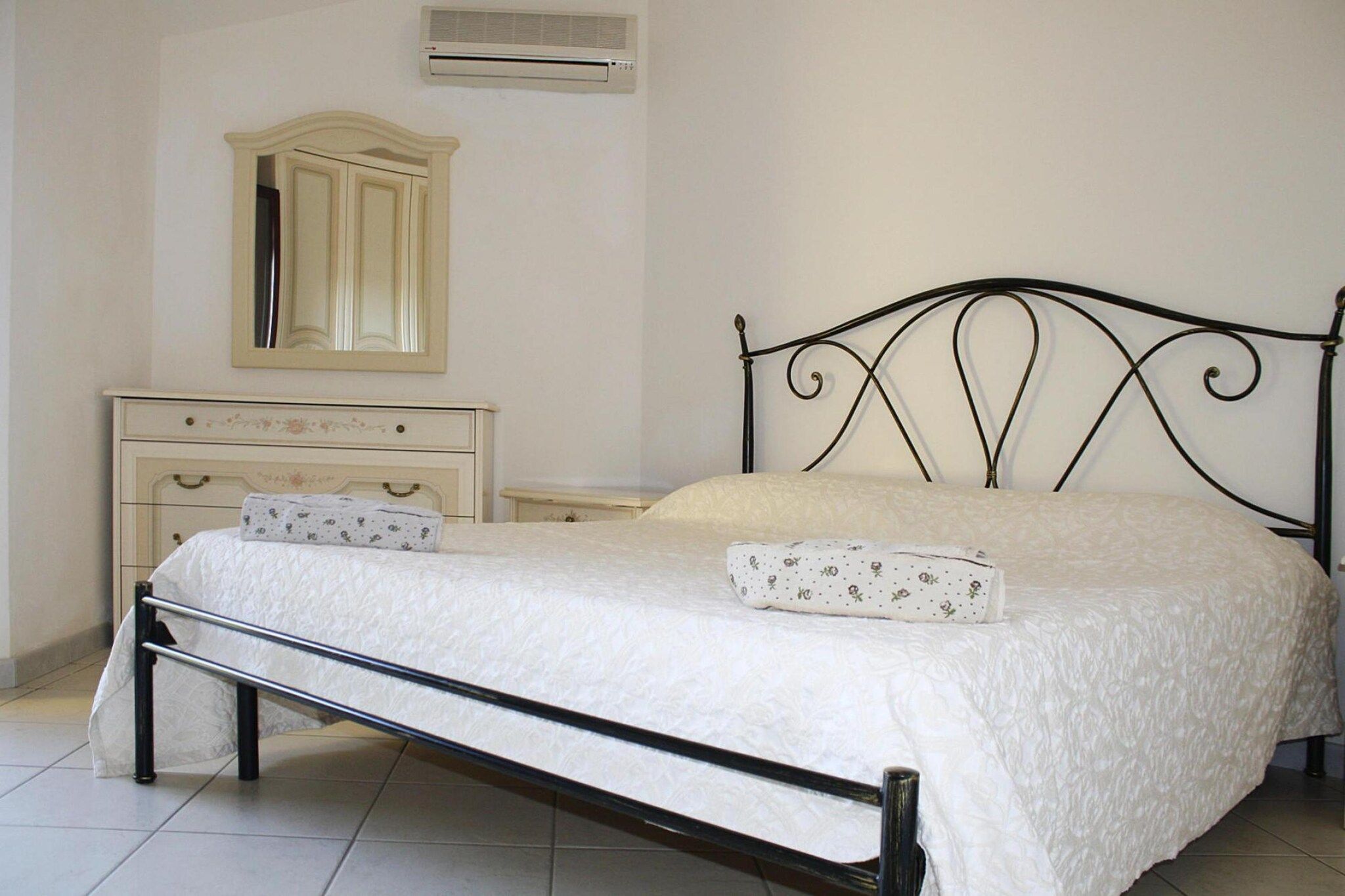 A bed with a metal frame, a bedside table, a dresser, and a mirror.