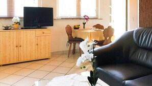 Un salon avec un canapé en cuir noir, un meuble en bois et un téléviseur. On y trouve également une table à manger avec des chaises et un vase de fleurs.