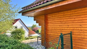 Une cabane en bois avec un toit en tuiles, entourée de verdure et d’autres bâtiments.