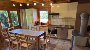 Une table de salle à manger en bois, avec des chaises, une cuisine dotée de meubles blancs, une cuisinière et une fenêtre donnant sur un paysage verdoyant.