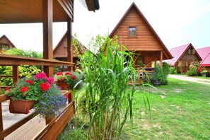 Una cabaña de madera con porche, rodeada de un jardín cuidado con diversas plantas y flores.