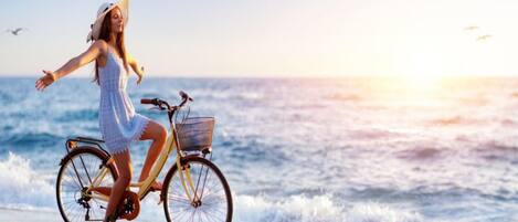 A person riding a bicycle with a basket on a beach with the ocean in the background.