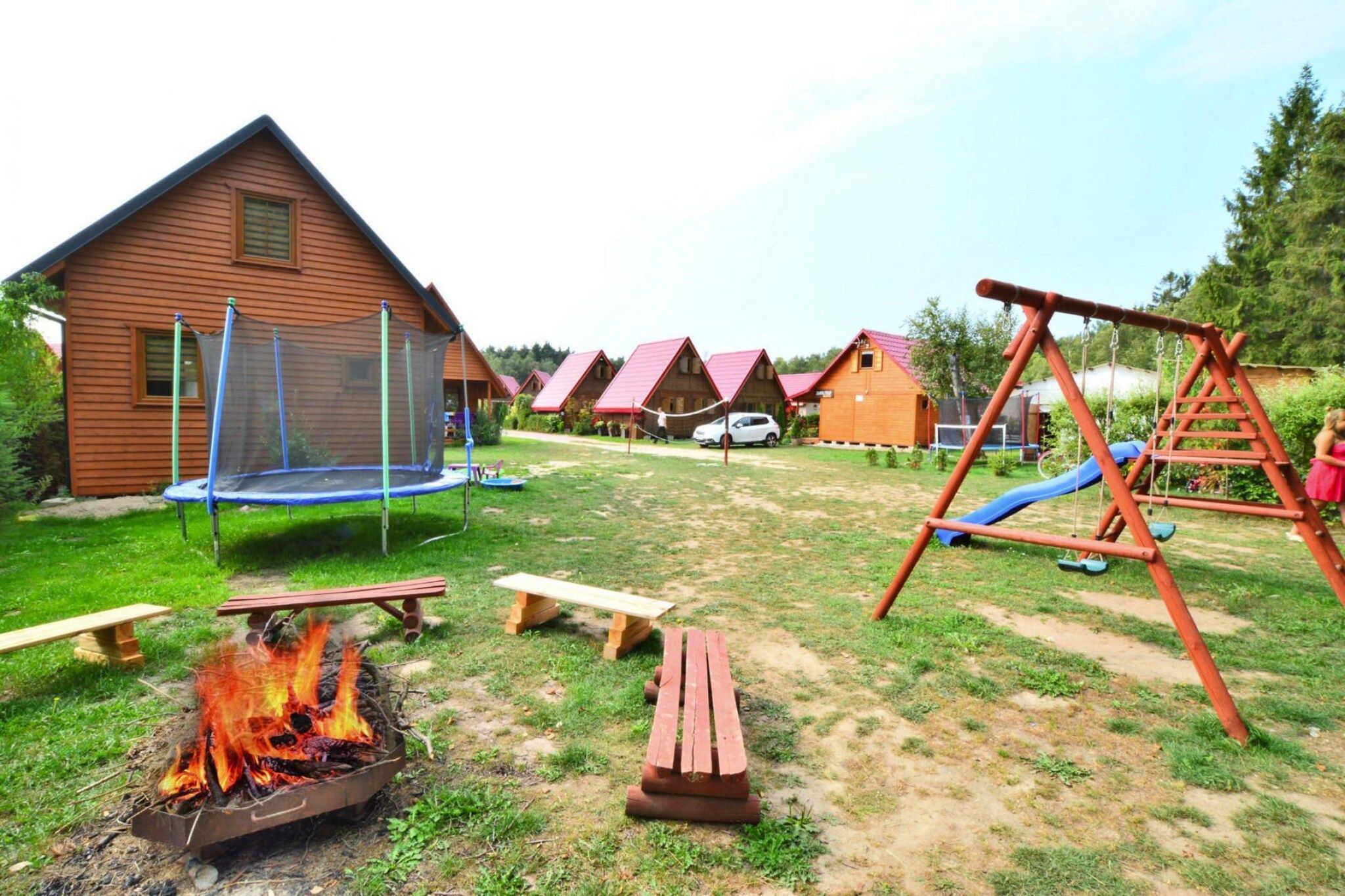 Un terrain de camping équipé d’un trampoline, d’aires de jeux en bois et d’un foyer de camp.