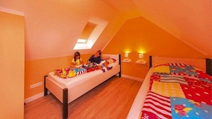 Un dormitorio con techo inclinado, una cama con colcha colorida, una mesita de noche con lámpara y una ventana pequeña.