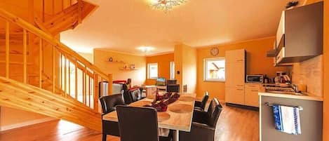 A modern kitchen with wooden flooring, a dining area with a wooden staircase, and a small island with a microwave.