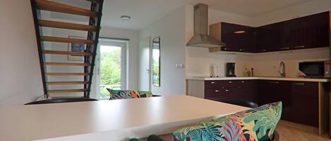 A modern kitchen with dark cabinets, a white countertop, and a microwave. There is a dining table with colorful chairs and a wooden chair with a backrest.