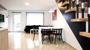 A modern living space with a dining area, a staircase, and a large window. - Reihenhaus am Gardersee (Lohmen)
