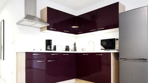 A modern kitchen with dark cabinets, a stainless steel range hood, a microwave, and a refrigerator. - Reihenhaus am Gardersee (Lohmen)