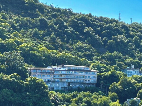 Um edifício de vários andares com varandas, rodeado por árvores verdes exuberantes numa encosta.
