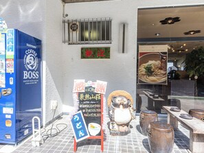 Fachada com uma máquina de café automática, uma placa com texto em japonês e uma figura decorativa de cerâmica.
