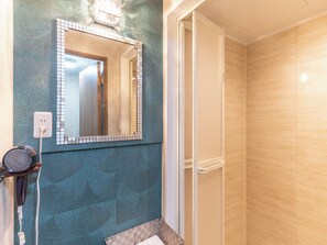 Casa de banho com parede revestida em azulejos, espelho, secador de cabelo e zona de duche.