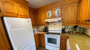 A kitchen with wooden cabinets, a white refrigerator, a stove, and a microwave. - Country Chalet with Lakefront (Chertsey)