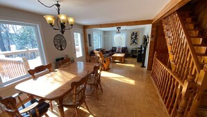 A spacious dining area with a large wooden table and chairs, a chandelier, and a view of the outdoors through large windows. - Country Chalet with Lakefront (Chertsey)