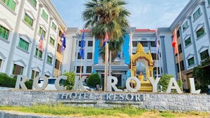 En hotelindgang med skiltet "ROCK ROYAL HOTEL & RESORT", palmer og flag.