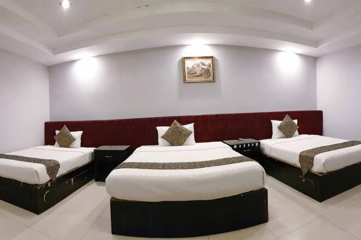 Una habitación de hotel con tres camas, un cabecero rojo y un cuadro en la pared.