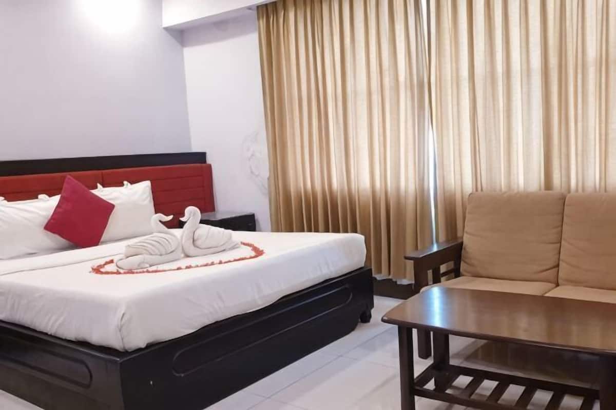 Una habitación de hotel con cama, sofá, mesa de madera y cortina.