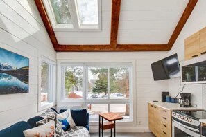 A compact kitchen with a built-in oven, a dining table, and a TV mounted above it. - Modern Cottage in the Tremblant Ski Village (Mont-Tremblant)