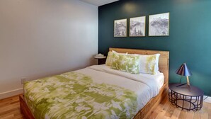 Un dormitorio con una cama, una mesita de noche, una lámpara y tres cuadros en la pared.