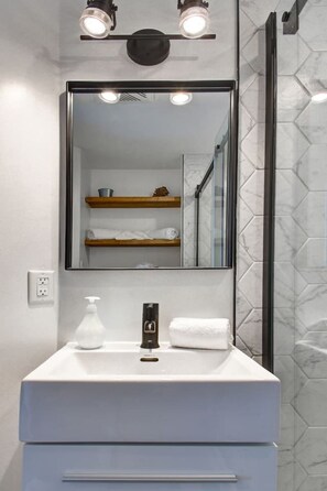 Une salle de bain moderne avec un meuble-lavabo blanc, un miroir doté d’un éclairage intégré, un distributeur de savon et une serviette.