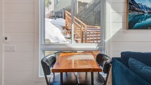 Una habitación con una mesa y sillas de madera, un sofá azul y una ventana con vistas a un paisaje nevado.
