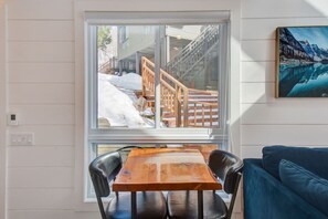 A room with a wooden table and chairs, a blue sofa, and a window with a view of a snowy outdoor area.