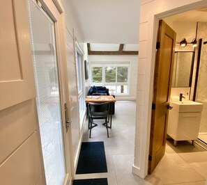 A hallway with a dining area, a wooden door leading to a bathroom, and a view of the outdoors through large windows. - Modern Cottage in the Tremblant Ski Village (Mont-Tremblant)