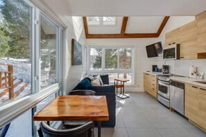 A modern kitchen with a dining area, large windows, and a TV. - Modern Cottage in the Tremblant Ski Village (Mont-Tremblant)