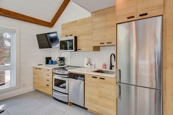 Une cuisine moderne dotée de meubles en bois, d’appareils électroménagers en acier inoxydable, d’un téléviseur à écran plat et d’une fenêtre laissant entrer la lumière naturelle.