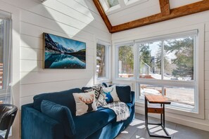 A cozy room with a blue sofa, a painting of a mountain landscape, and large windows offering a view of the outdoors. - Modern Cottage in the Tremblant Ski Village (Mont-Tremblant)
